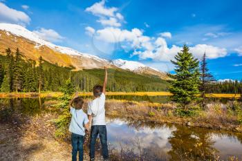 Two boys stand on the coast of the marshy lake. The concept of active tourism. Rocky Mountains on a sunny day