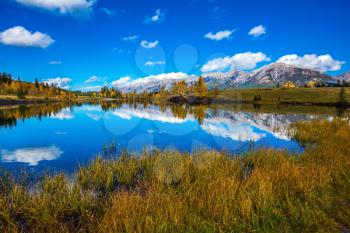 The concept of hiking. Bright shining autumn day in Canmore, near Banff National Park. Majestic mountains and scenic cumulus clouds are reflected in the lake