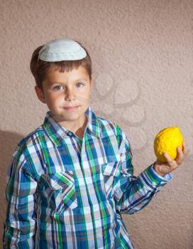 Adorable Jewish boy wearing a white skull cap holds a ritual fruit - Etrog. Sukkot
