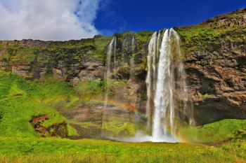 Seljalandsfoss waterfall in Iceland. Sunny day in July. Large rainbow decorates a drop of water