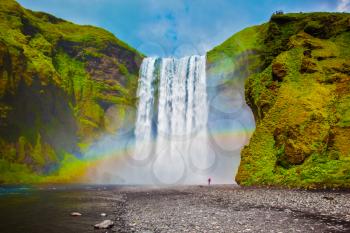 The most popular waterfall in Iceland - Skogafoss. Water rushes down with a crash, forming a cloud of mist. Picturesque huge rainbow appears in the water mist