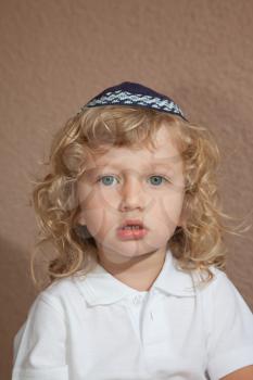 The charming little boy with long blond curls and blue eyes in the Jewish knitted skullcap. Autumn holiday of Sukkot
