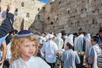 The Jewish holiday of Sukkot. Adorable little boy with long blond curls and blue eyes in blue skullcap. He stands at Western Wall of Temple