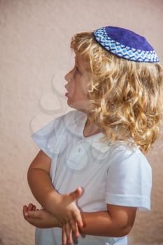 The charming little boy with long blond curls and blue eyes in the Jewish knitted yarmulke. Autumn holiday of Sukkot