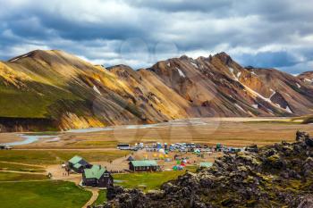 Iceland in July. Great Valley Park Landmannalaugar, surrounded by mountains of rhyolite and unmelted snow. In the valley built large camp. The concept of world tours. Trend Around the World