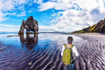 Woman with a green backpack admires Rock Hvitsercur. Northern coast of Iceland. Concept of extreme northern tourism