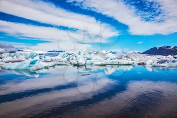 Magnificent summer morning in the ocean gulf with floating ice floes. The layered clouds fanning are reflected in a smooth surface of water. Ice lagoon in Iceland