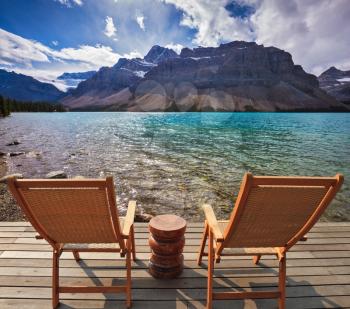 Cold autumn day in the Rocky Mountains of Canada. On the wooden platform there are two deckchairs beside a beautiful lake