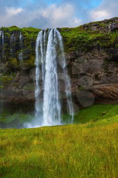 Seljalandsfoss waterfall in July. Large rainbow decorates a drop of water. Sunny day in Iceland