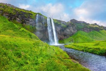 The warm July day in Iceland. Seljalandsfoss waterfall. Rainbow decorates drop of water
