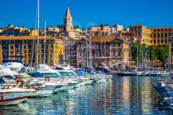The blue water reflects the ancient buildings on the waterfront. Rows of sailing yachts, motor boats and fishing boats. The Marseille Old Port
