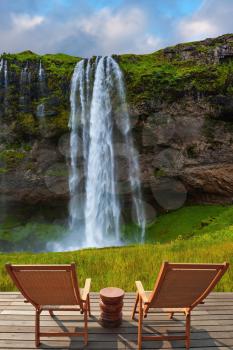 The warm July day in Iceland. Seljalandsfoss waterfall. Deck chairs on the wooden floor waiting for tourists
