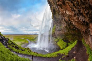 Seljalandsfoss waterfall in July. Passage under the waterfall. Sunny day in Iceland. Photo taken fisheye lens