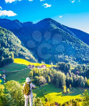 Elderly woman - tourist with backpack travels and takes pictures in Tyrol. Warm autumn in the Val de Funes, Dolomites. The concept of active and ecotourism