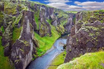  Steep vertical cliffs surround the stream of very cold water. Fantastic canyon in Iceland - Fyadrarglyufur. The concept of northern tourism