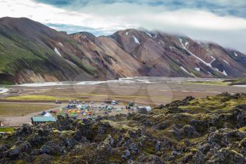 The valley is large tourist camp. Pink and green rhyolite mountains surround the flat valley of the National Park Landmannalaugar