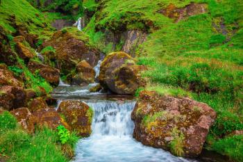 Iceland. Basalt mountains covered in green grass and moss. Gorgeous cascading waterfall from melting glacier