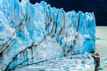 Woman photographs phenomenon of nature - the blue ice wall. The fantastic glacier Perito Moreno, in the Patagonia. The concept of exotic and extreme tourism