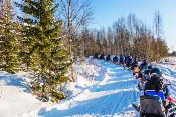 Concept of active winter tourism. Snowmobiling. Tourist train from snowmobiles moves along the ice of a frozen river