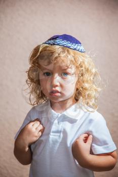 The charming little boy with long blond curls and blue eyes in Jewish knitted kippah