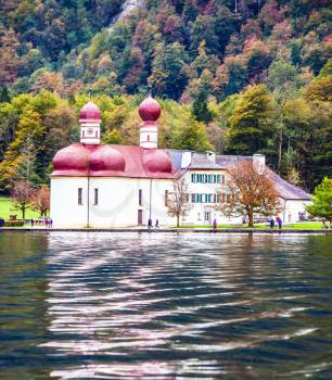 Magic Monastery of St. Bartholomew at Lake Königssee. Red domes of the church reflected in the water. Picture taken from on board tourist boats. The concept of active tourism