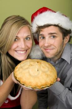 Royalty Free Photo of a Couple Holding a Pie and the Man's in a Santa Hat