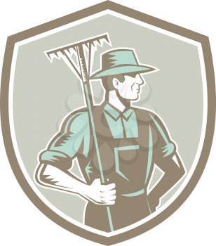 Illustration of organic farmer holding rake on shoulder facing side set inside shield crest on isolated background done in retro woodcut style.