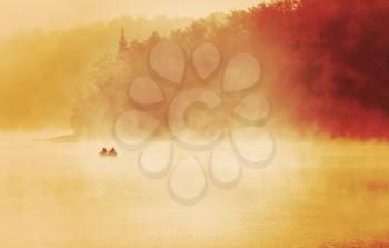 Exuding fishermen fishing in a lake, early misty foggy morning dramatic sunlight