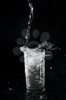 Water being poured in a transparent glass on the black background