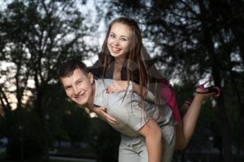 Young loving couple piggybacking in the park in the evening sunset