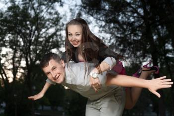 Young loving couple piggybacking in the park in the evening sunset