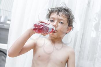 Little kid is drinking red water indoors, horizontal shot