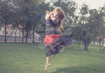 The young female jumps on a green grass in evening time in city park . Girl jumping like flying bird.