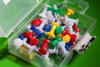 closeup shot of mixed colors office push-pins in the open plastic pack, angle view, on the green background