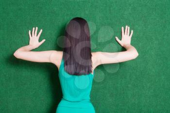 Torso shot of the pretty female weared green dress. 20s brunete lady against green wall from back
