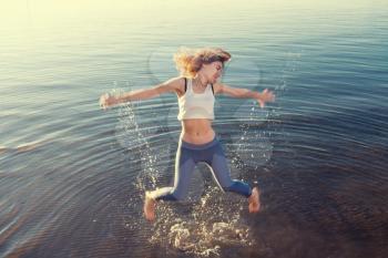 Summertime fun. Outdoor portrait of young beautiful blonde woman jumping in water