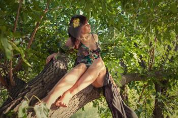 Sensual girl with long healthy hair sitting on a tree outdoors.