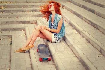 Redhead women sitting on a stairs  with her skateboard in sunglasses.