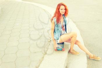 Red haired girl sitting on  her scateboard