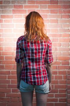 Back side view of a redhead female befor red brick wall