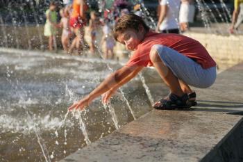 Cute boy in red shirt  playing with water outdoorson parapet of city park fountain