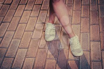 White sneakers on girl legs on the pavement with shadows. Legs crossed ready for jogging, copyspace.