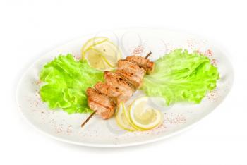 salmon kebab at plate with green lettuce and lemon on a white