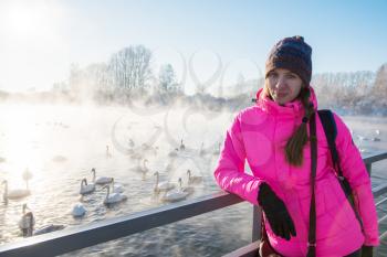 Woman at winter nonfreezing lake with white whooping swans. The place of wintering of swans, Altay, Siberia, Russia.