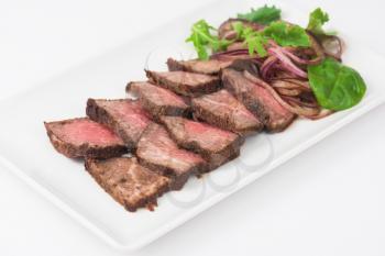 Plate with meat cutting and fresh greens on white plate