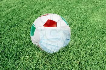 Soccer ball in italian colors with mask on green field. Virus threatened championship concept