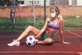 A young beauty athletic woman in sportswear with soccer ball in protective mask. Virus threatened soccer concept