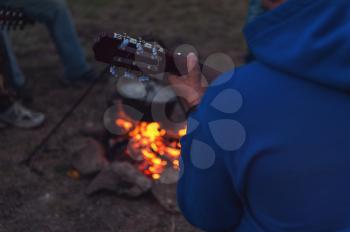 Closeup photo of the man playing o guitar near the campfire