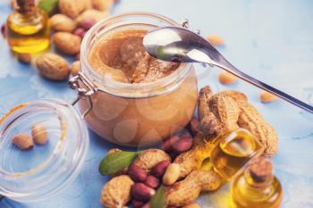 Natural peanut butter with oil in a glass jar and peanuts
