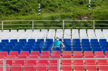 Lonely boy in protective mask on the empty stadium outdoor. Empty tribune due to pandemic Covid-19. Concept of pandemic life , empty stadiums, distance from viewers, safety.